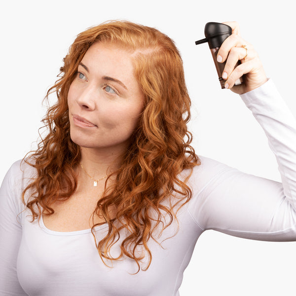 Woman with light reddish-brown hair with thin hair on her parting line using the spray applicator